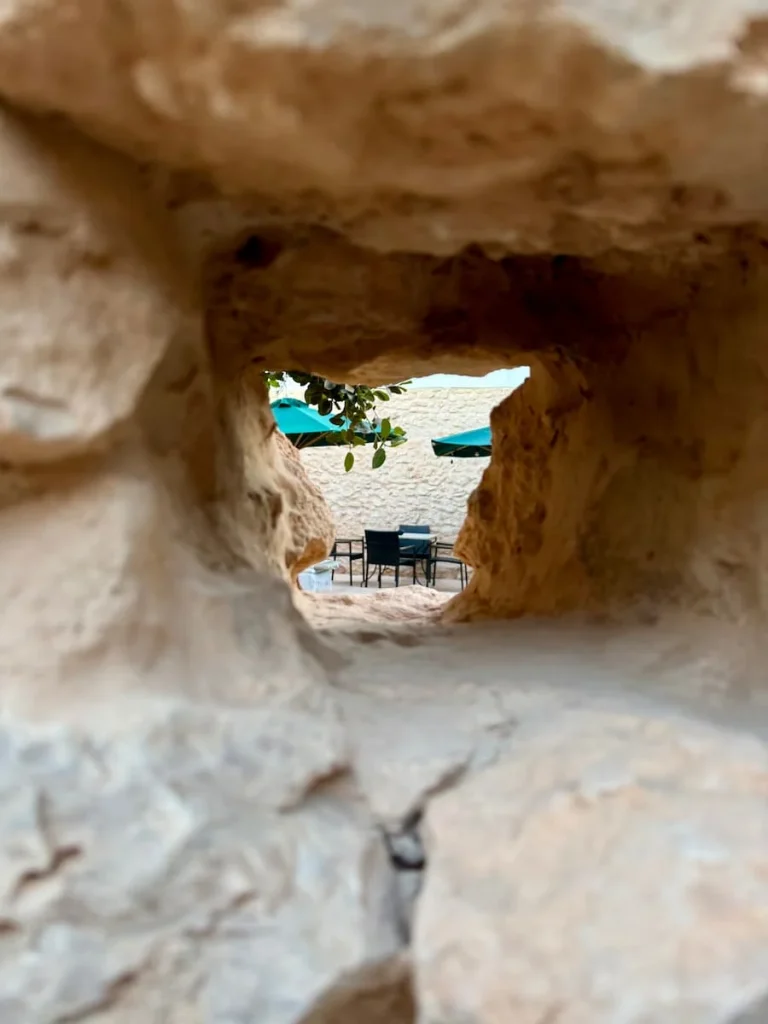 View of outdoor seats and green umbrellas through stone work at Dar Dhiafa in Djerba