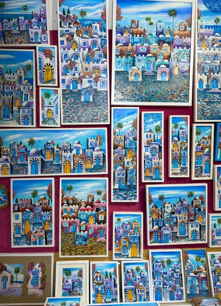 A collection of oblong water colour paintings on a red wall in a local souvenir shop, Sidi Bou Said, Tunisia
