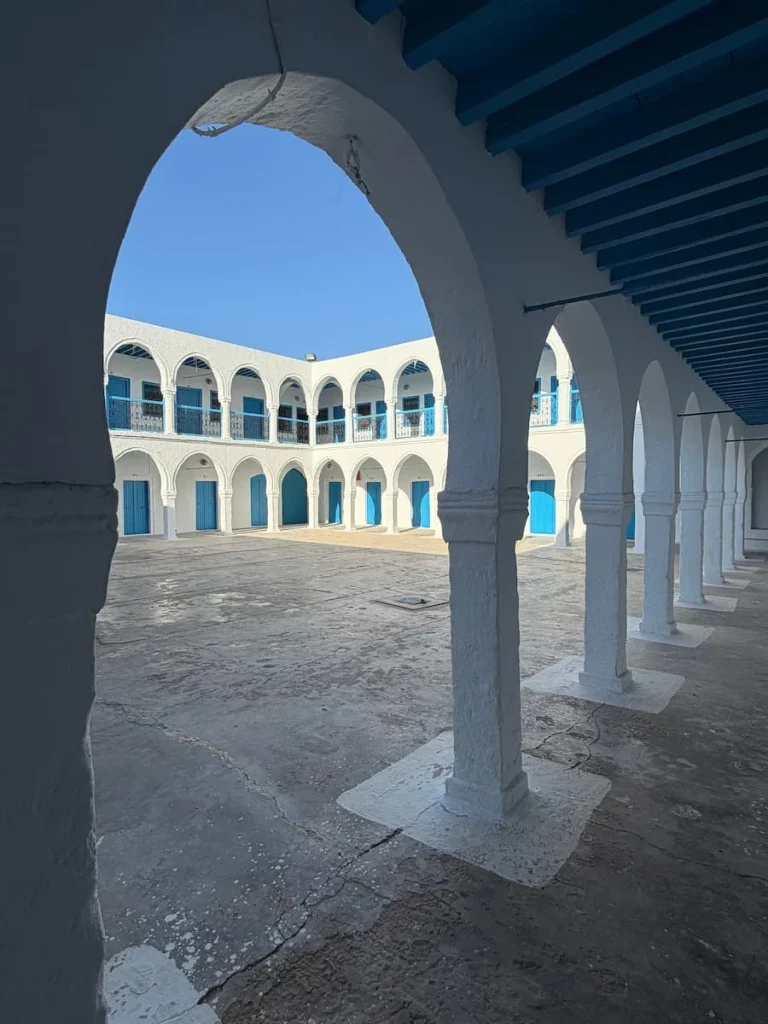 White and blue interior courtyard of El Ghriba Synagogue. The courtyard is clear of people and the blue sky is peeping through