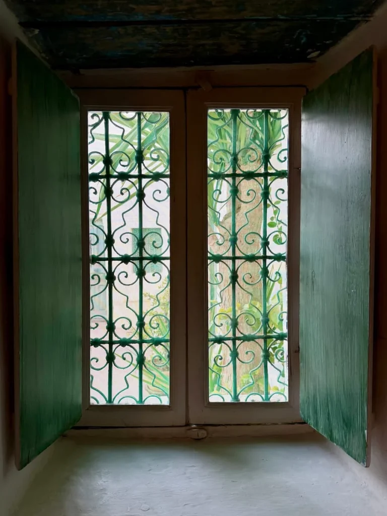 A pale green and wood windown at Dar Dhiafa, Djerba. there are wrought iron patterns on the window reflecting the light into the room