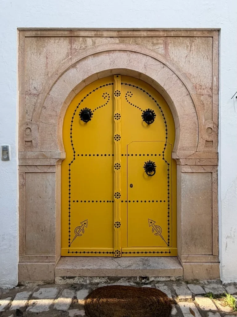 Golden studded doorway with a light browb background and steps leading up to it in Sidi Bou Said, Tunisia