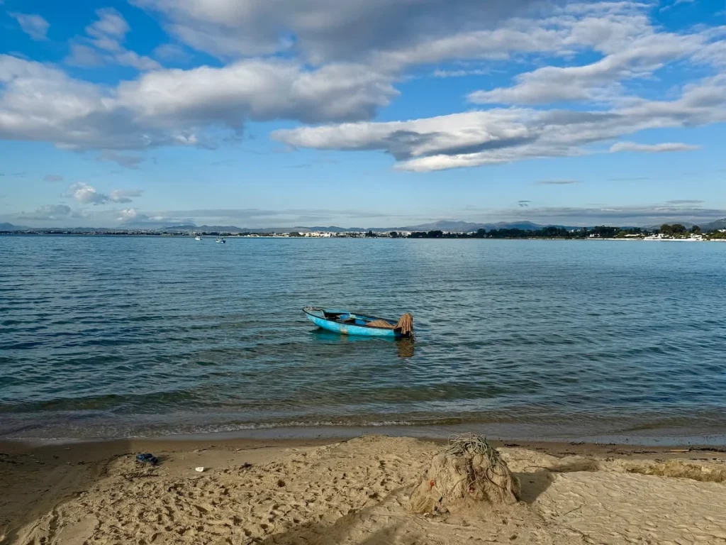 Hammamet Plage with a light blue fishing boat in the sea close to the shore and rocks in the background