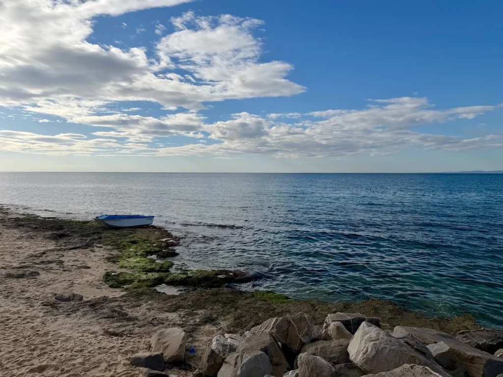 Hammamet Plage with rocks, fishing boat and sea. The clouds are low adn cotton wool like
